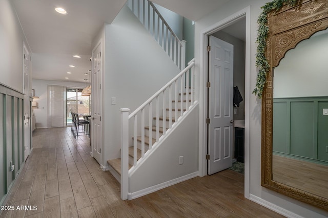 stairway with a wainscoted wall, recessed lighting, and wood finished floors