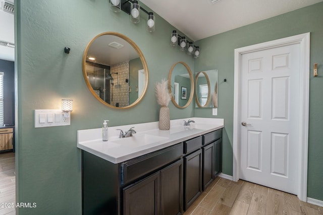 full bathroom featuring visible vents, a sink, wood finished floors, double vanity, and baseboards