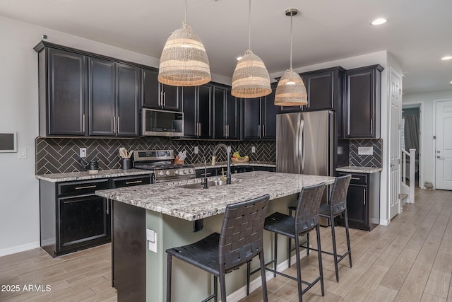 kitchen with a kitchen bar, a sink, dark cabinetry, light wood-style floors, and appliances with stainless steel finishes