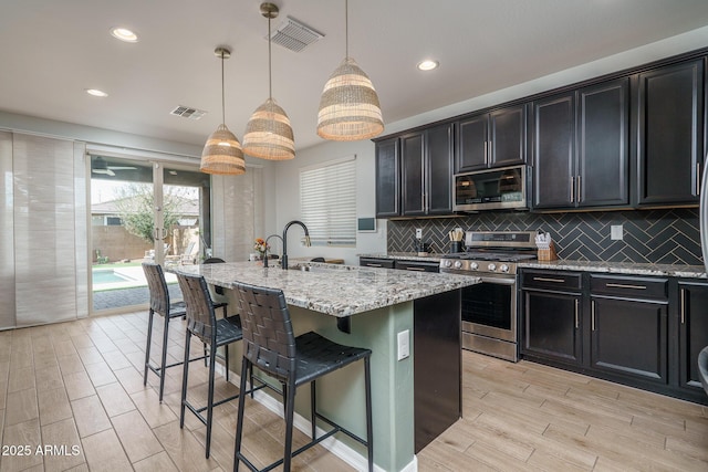 kitchen featuring dark cabinets, a kitchen bar, light stone counters, stainless steel appliances, and a sink