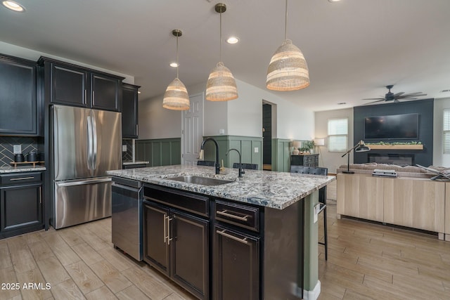 kitchen with wood finish floors, a sink, ceiling fan, stainless steel appliances, and open floor plan