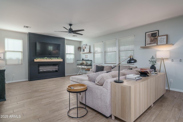 living area with light wood-type flooring, visible vents, a large fireplace, baseboards, and ceiling fan