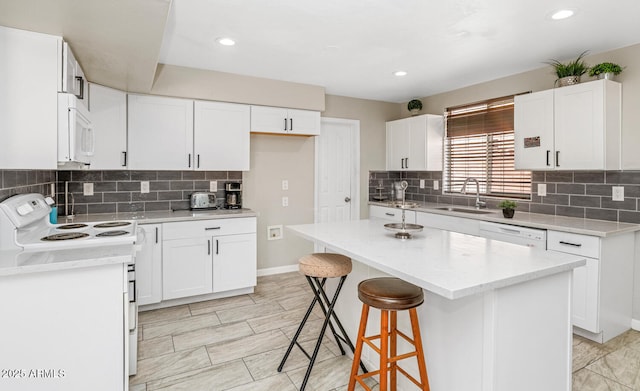 kitchen with white appliances, a sink, a center island, backsplash, and a breakfast bar area