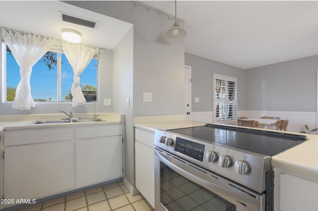 kitchen with stainless steel electric stove, sink, light tile patterned floors, decorative light fixtures, and white cabinetry