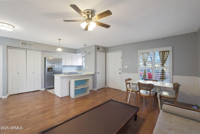 kitchen featuring kitchen peninsula, stainless steel refrigerator with ice dispenser, hardwood / wood-style flooring, white cabinets, and hanging light fixtures