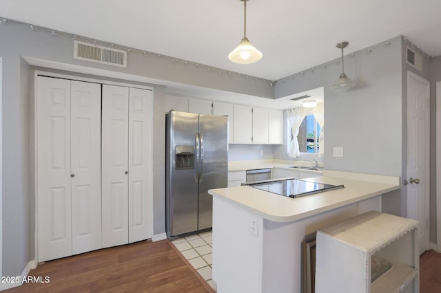 kitchen featuring kitchen peninsula, appliances with stainless steel finishes, a kitchen bar, white cabinetry, and hanging light fixtures