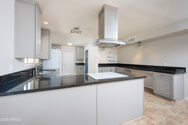 kitchen with island exhaust hood, a sink, dark stone counters, white appliances, and a peninsula