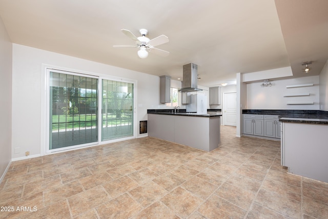 kitchen with a ceiling fan, dark countertops, a peninsula, island exhaust hood, and gray cabinets