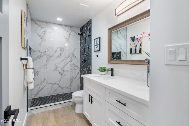 bathroom with vanity, wood-type flooring, tiled shower, and toilet