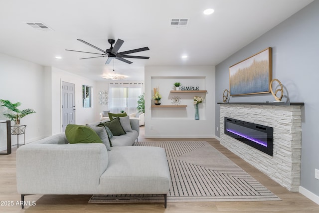 living room with a stone fireplace, ceiling fan, and light hardwood / wood-style floors