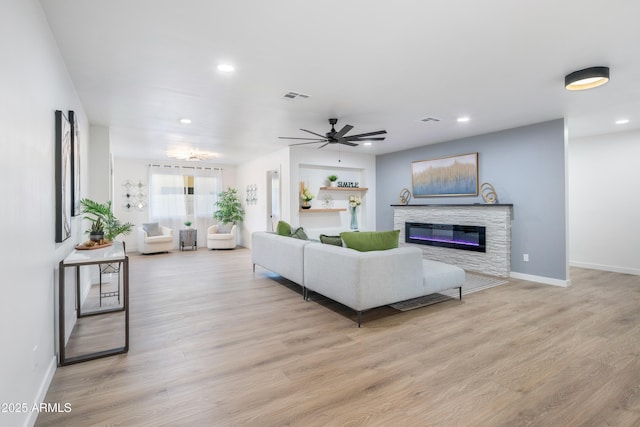 living room featuring ceiling fan, a stone fireplace, and light wood-type flooring