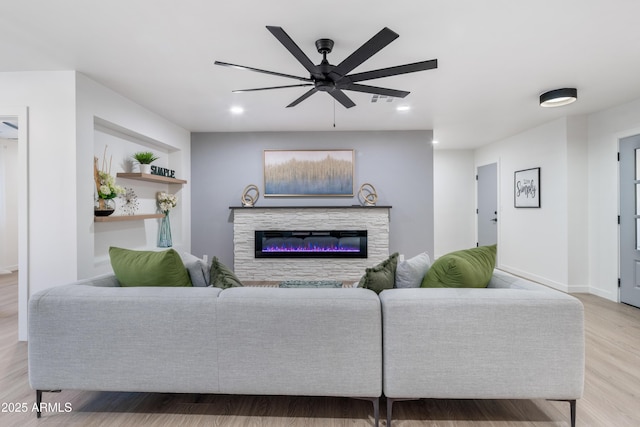 living room with ceiling fan, a stone fireplace, and light wood-type flooring