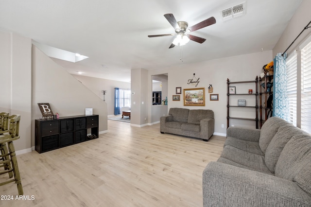 living room with ceiling fan, a skylight, and light wood-type flooring