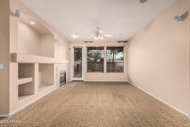 unfurnished living room with baseboards, a tiled fireplace, ceiling fan, carpet floors, and built in shelves