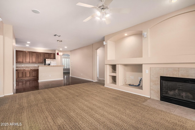 unfurnished living room with built in features, arched walkways, dark colored carpet, visible vents, and a tile fireplace