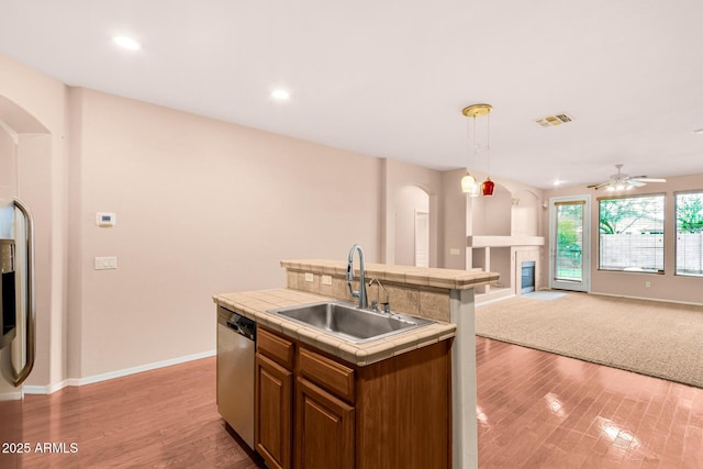 kitchen with visible vents, tile counters, a glass covered fireplace, stainless steel dishwasher, and a sink