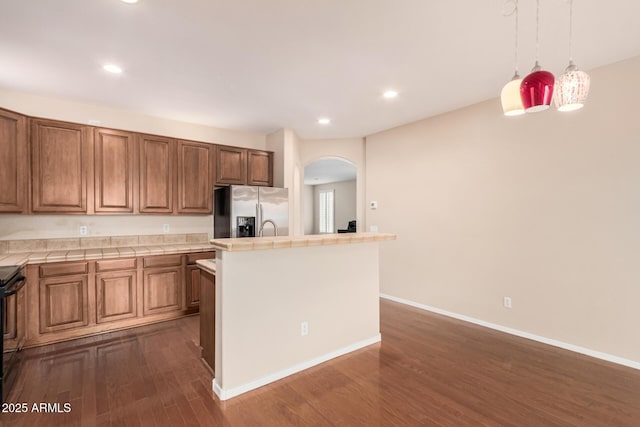 kitchen featuring stainless steel refrigerator with ice dispenser, dark wood finished floors, tile counters, and a center island with sink