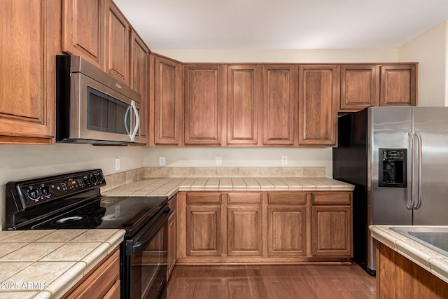 kitchen with appliances with stainless steel finishes, brown cabinets, and tile countertops