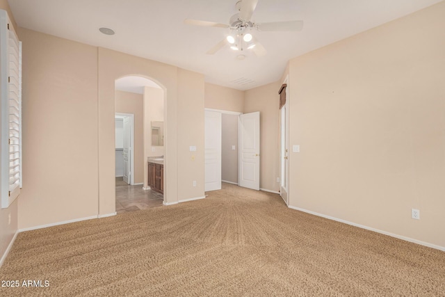 unfurnished bedroom with arched walkways, carpet flooring, and baseboards