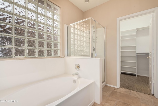 full bathroom with a spacious closet, a shower stall, a bath, and baseboards