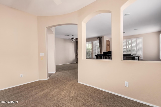 spare room with carpet floors, baseboards, arched walkways, and a ceiling fan