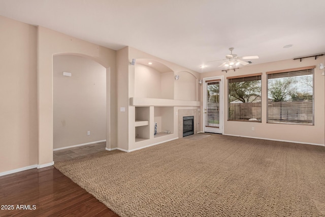 unfurnished living room with built in features, baseboards, arched walkways, a ceiling fan, and a fireplace