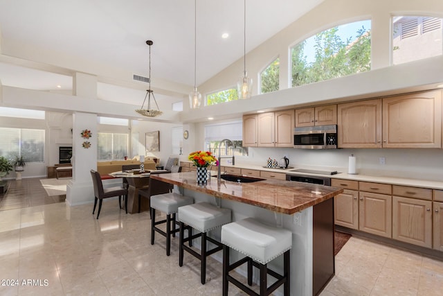 kitchen featuring a breakfast bar, sink, light stone countertops, an island with sink, and high vaulted ceiling