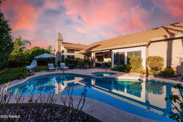 pool at dusk with an in ground hot tub and a patio area