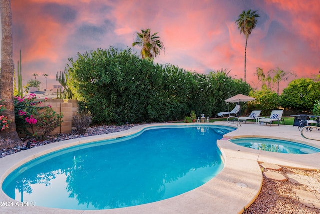 pool at dusk featuring an in ground hot tub and a patio