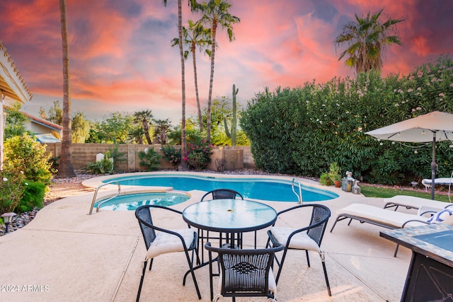 pool at dusk featuring an in ground hot tub and a patio