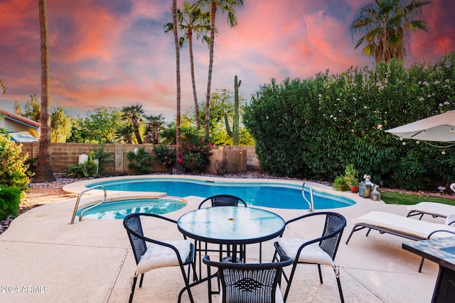 pool at dusk with an in ground hot tub and a patio