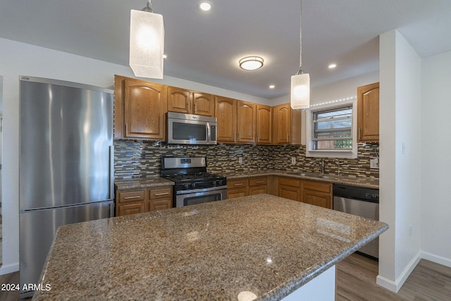 kitchen with appliances with stainless steel finishes, hardwood / wood-style flooring, dark stone counters, and hanging light fixtures