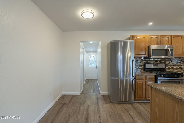kitchen with backsplash, dark stone countertops, stainless steel appliances, baseboards, and dark wood-style floors