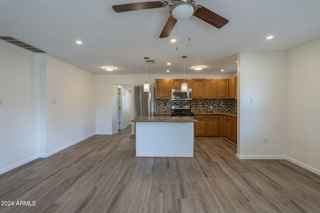 kitchen with visible vents, wood finished floors, stainless steel appliances, decorative backsplash, and a kitchen island