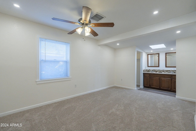 unfurnished living room with ceiling fan, light colored carpet, and a skylight