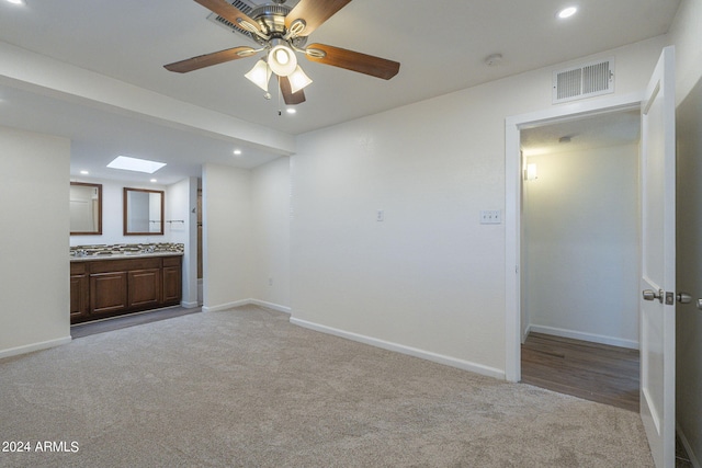 interior space with light colored carpet, a skylight, and ceiling fan