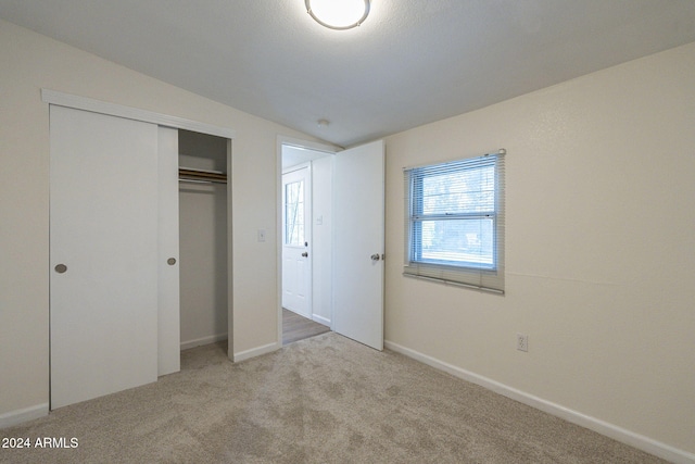 unfurnished bedroom featuring lofted ceiling, a closet, and light colored carpet