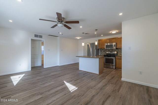 kitchen featuring tasteful backsplash, open floor plan, dark countertops, stainless steel appliances, and wood finished floors