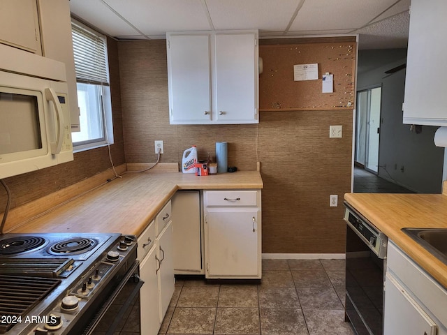 kitchen featuring black appliances, a drop ceiling, white cabinets, and dark tile patterned flooring