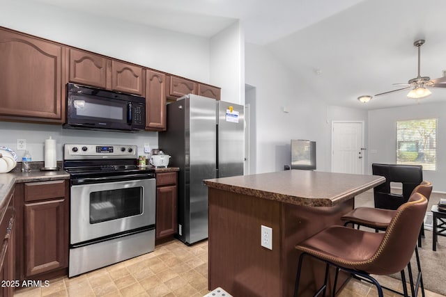 kitchen with vaulted ceiling, a kitchen bar, a center island, ceiling fan, and stainless steel appliances