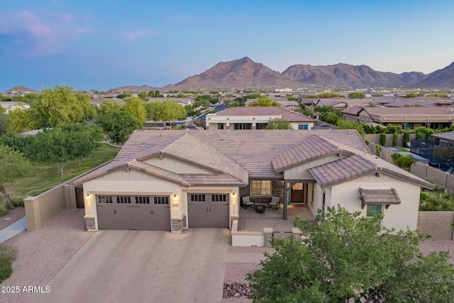 mediterranean / spanish home featuring a mountain view, stone siding, aphalt driveway, a garage, and a tiled roof