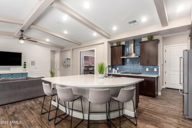 kitchen with wall chimney range hood, open floor plan, dark brown cabinets, visible vents, and a breakfast bar area