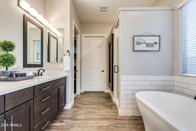 full bath with a freestanding tub, double vanity, a stall shower, a sink, and wood finished floors