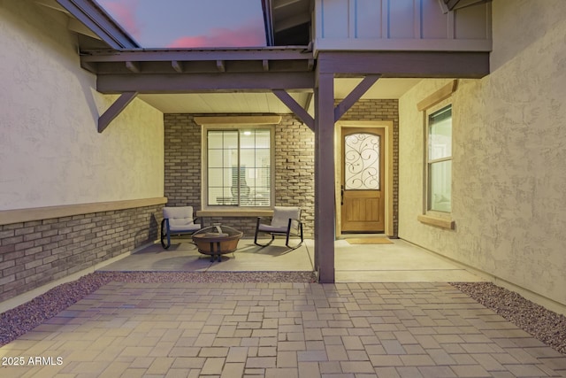 doorway to property with a patio area, brick siding, stucco siding, and board and batten siding