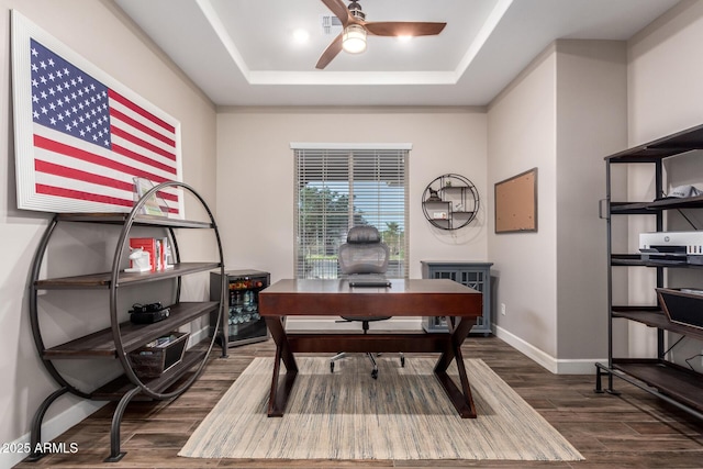 home office featuring a raised ceiling, ceiling fan, baseboards, and dark wood finished floors