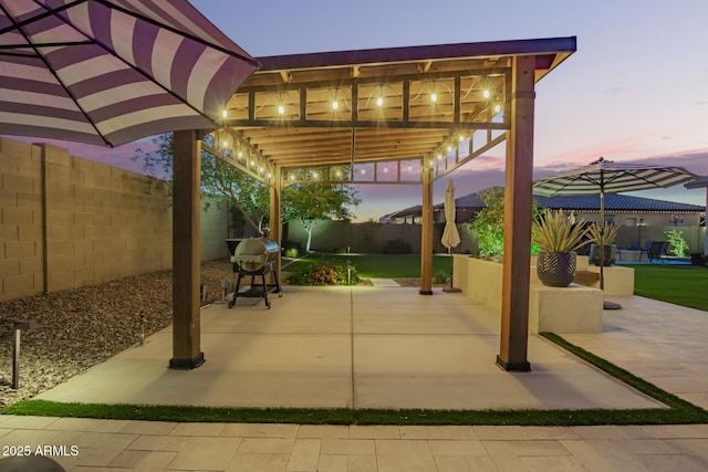 patio terrace at dusk with area for grilling, a fenced backyard, and a pergola