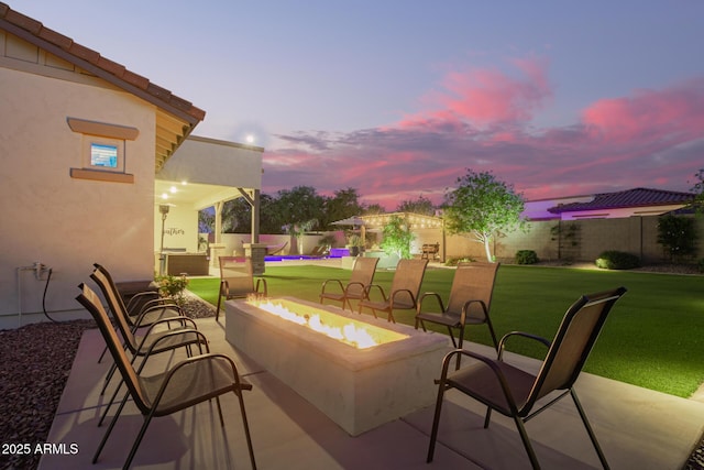 patio terrace at dusk featuring a yard, a fenced backyard, and an outdoor fire pit
