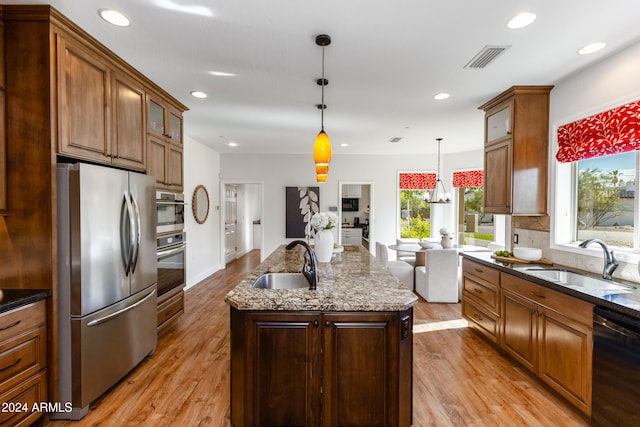 kitchen featuring sink, stainless steel appliances, hanging light fixtures, and an island with sink