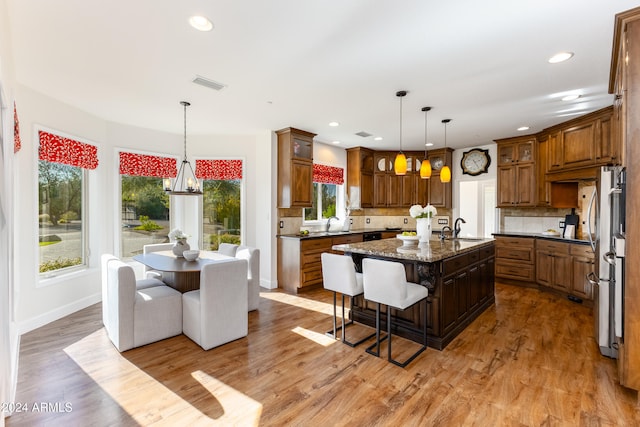 kitchen with plenty of natural light, dark stone countertops, decorative backsplash, and a kitchen island with sink