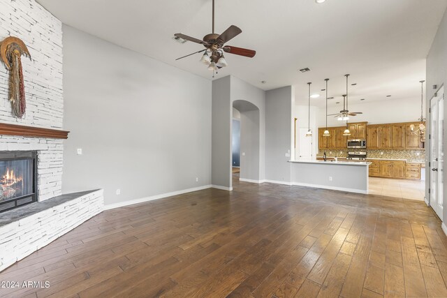 unfurnished living room with a stone fireplace, ceiling fan, and hardwood / wood-style floors